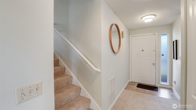 tiled entrance foyer with visible vents, stairway, and baseboards