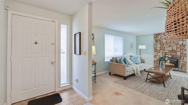 entrance foyer featuring a stone fireplace, light colored carpet, and baseboards