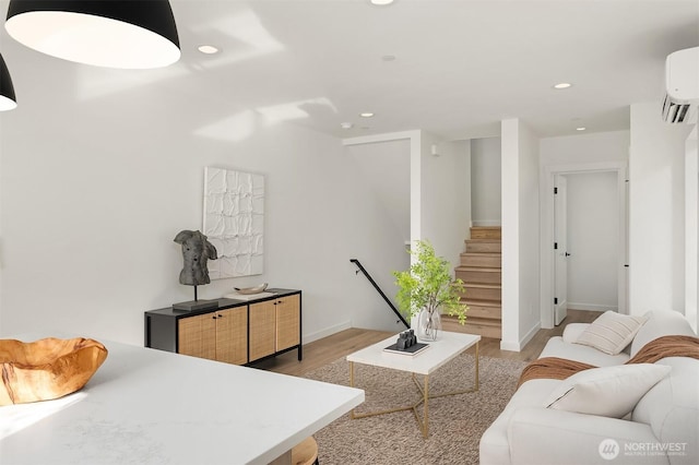 living room featuring an AC wall unit, recessed lighting, light wood finished floors, baseboards, and stairs