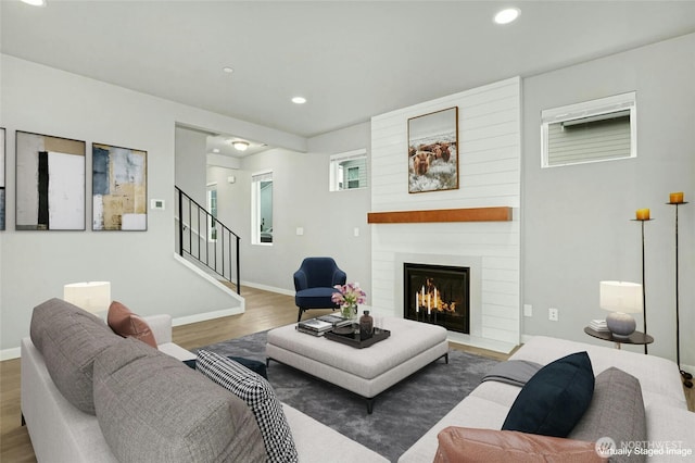 living area with a large fireplace, baseboards, stairway, recessed lighting, and wood finished floors