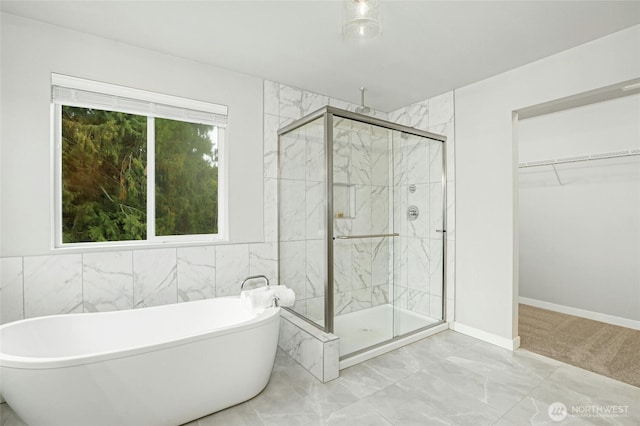 full bathroom featuring marble finish floor, plenty of natural light, a shower stall, a freestanding bath, and a spacious closet