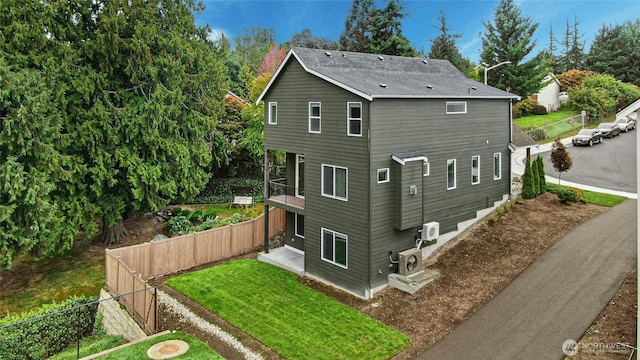 back of property with ac unit, fence, and a lawn