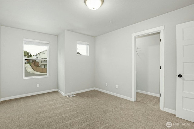 unfurnished bedroom featuring a spacious closet, baseboards, a closet, and light carpet