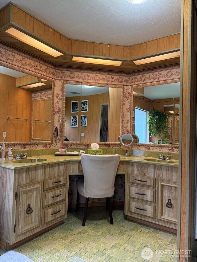 full bathroom featuring double vanity, wallpapered walls, and a sink