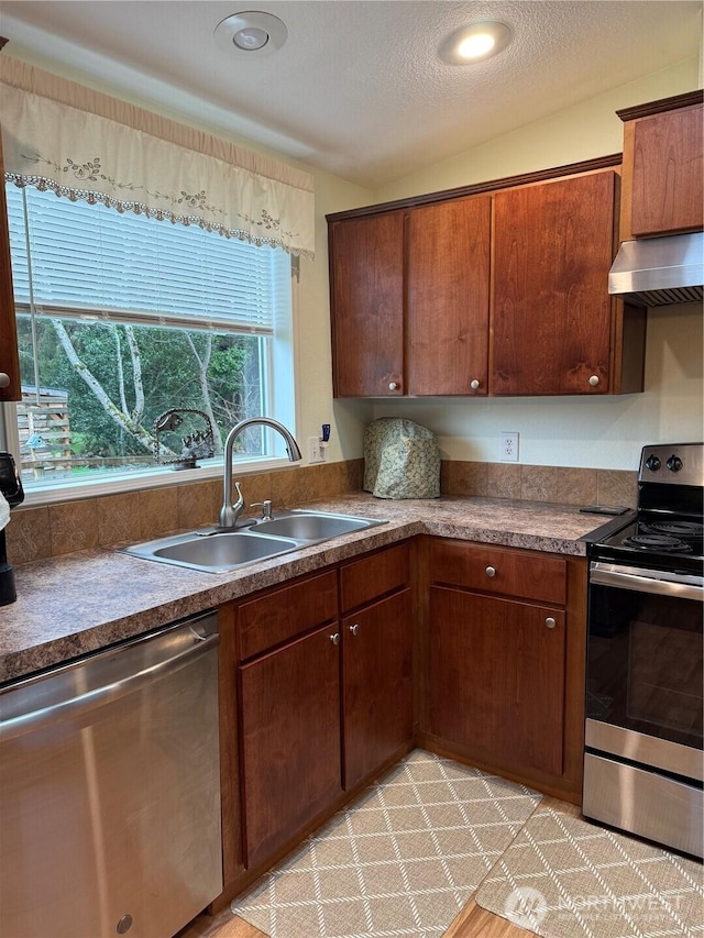 kitchen featuring dark countertops, ventilation hood, a textured ceiling, stainless steel appliances, and a sink