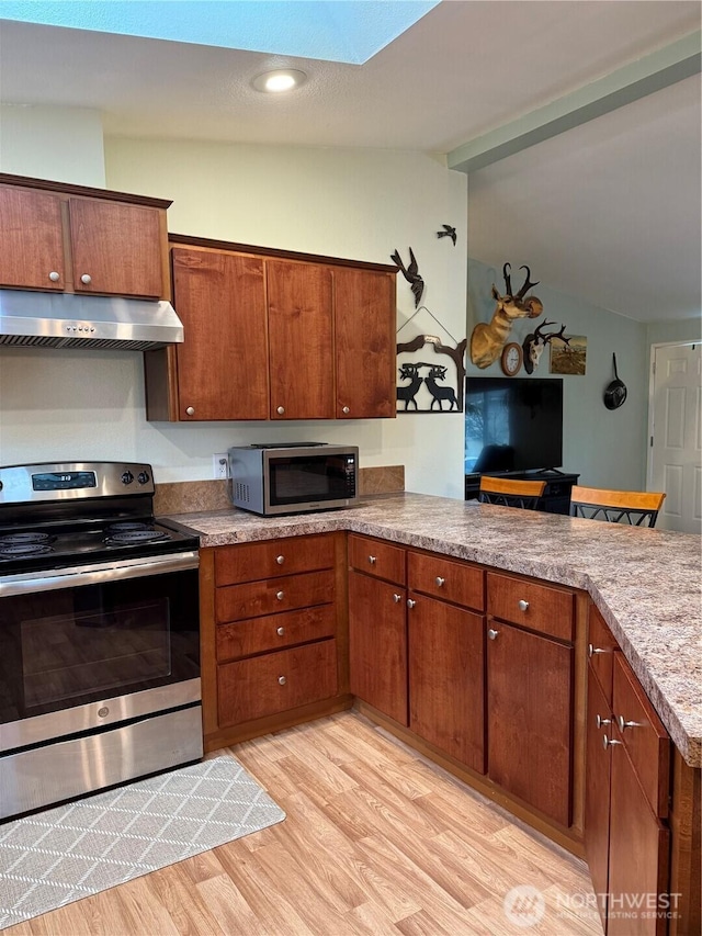 kitchen featuring a peninsula, vaulted ceiling, light wood-style floors, appliances with stainless steel finishes, and under cabinet range hood