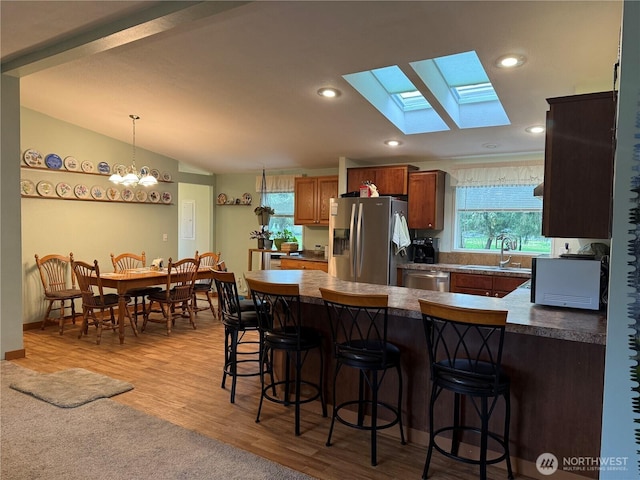 kitchen featuring a sink, vaulted ceiling with skylight, a peninsula, appliances with stainless steel finishes, and a breakfast bar area