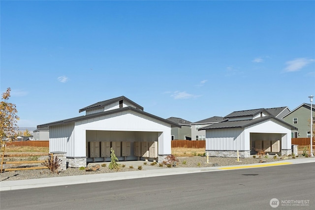 view of front of property featuring a standing seam roof, fence, stone siding, and metal roof