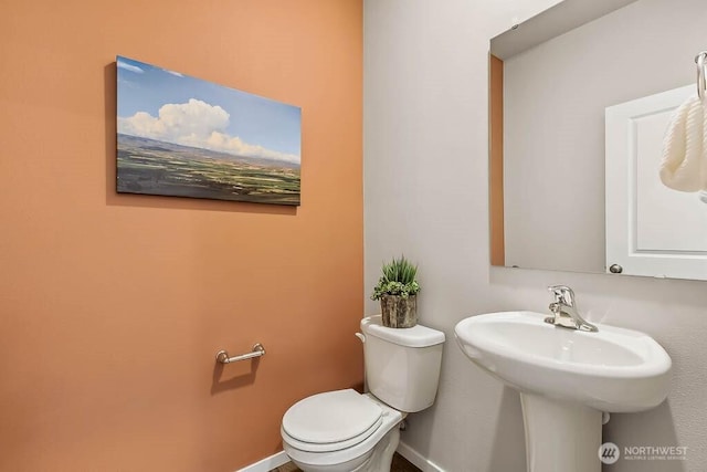 half bathroom featuring toilet, baseboards, and a sink