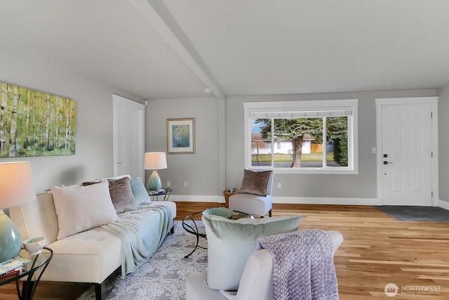 living area with beam ceiling, baseboards, and wood finished floors