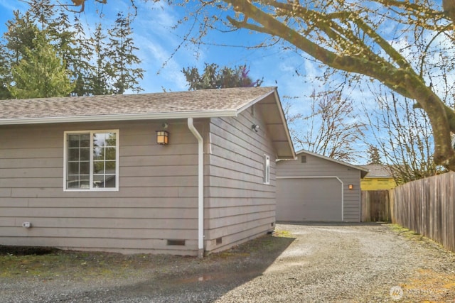 view of side of property with driveway, a detached garage, fence, an outdoor structure, and crawl space