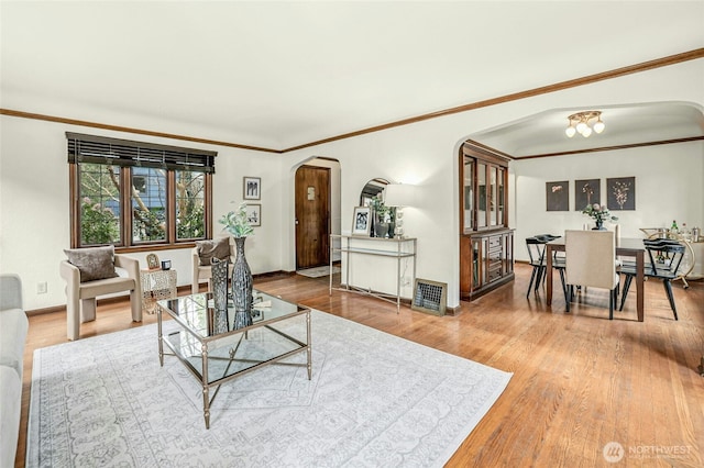 living area featuring crown molding, wood finished floors, arched walkways, and baseboards