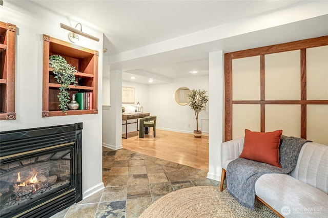 living room with a glass covered fireplace, stone tile floors, recessed lighting, and baseboards