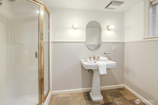 bathroom with visible vents, wainscoting, a shower stall, and stone finish floor