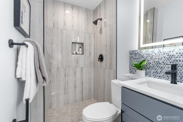 bathroom featuring decorative backsplash, toilet, tiled shower, and vanity