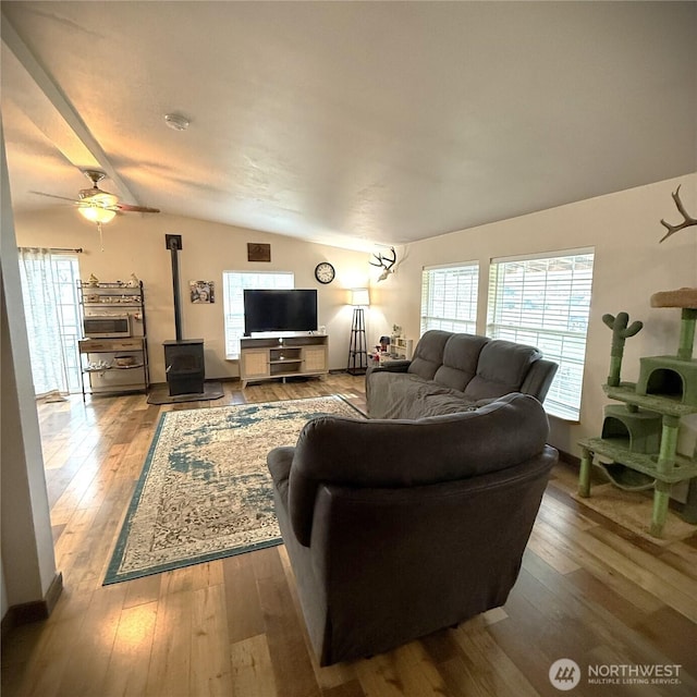 living area featuring hardwood / wood-style floors, lofted ceiling, a wood stove, and ceiling fan