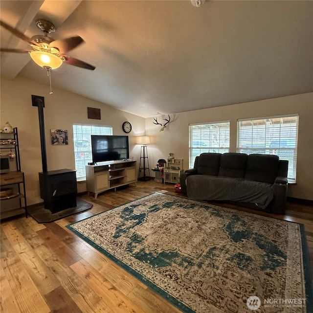 living area featuring a ceiling fan, vaulted ceiling, a wood stove, and wood finished floors