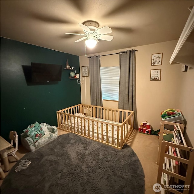 carpeted bedroom with a nursery area and a ceiling fan