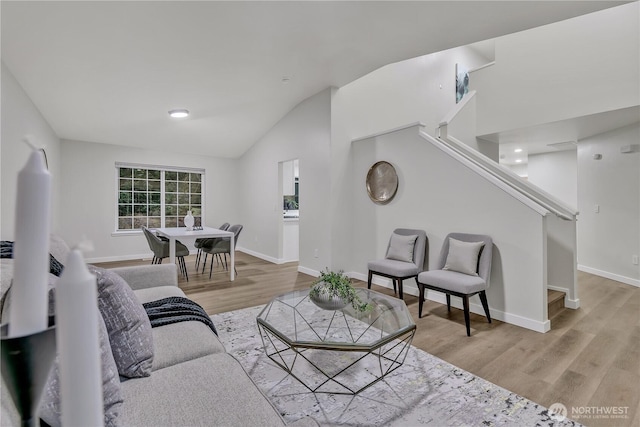 living room with baseboards, stairs, lofted ceiling, and light wood-style floors