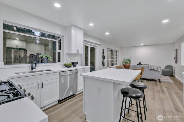 kitchen featuring light wood-type flooring, a sink, a kitchen island, stainless steel dishwasher, and a breakfast bar area