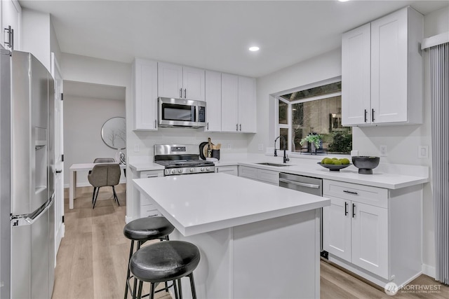 kitchen with light wood-type flooring, a breakfast bar, a sink, white cabinetry, and appliances with stainless steel finishes