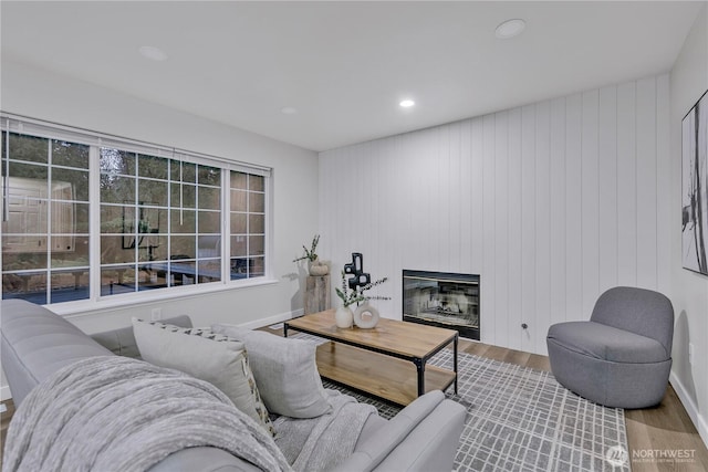 living room with a glass covered fireplace, recessed lighting, baseboards, and wood finished floors