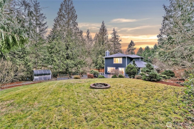 yard at dusk featuring an outbuilding, a greenhouse, and an outdoor fire pit