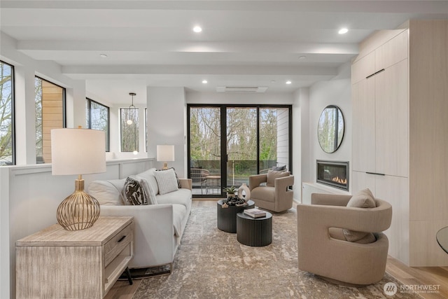 living area with a glass covered fireplace, beamed ceiling, visible vents, and wood finished floors