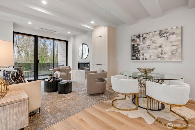 living area with beamed ceiling, visible vents, a glass covered fireplace, wood finished floors, and recessed lighting