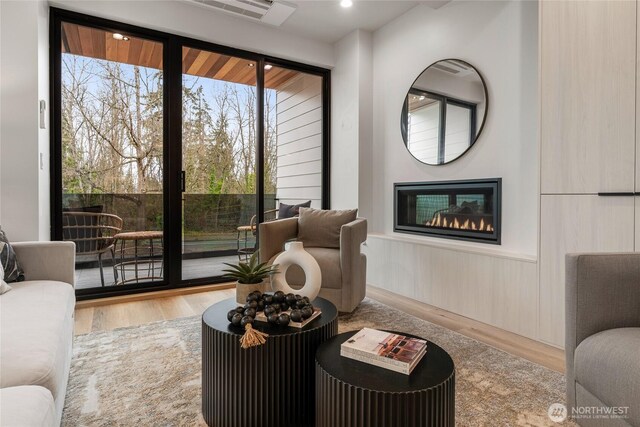 living area featuring a glass covered fireplace, wood finished floors, and a wainscoted wall