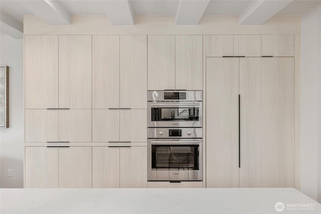 kitchen with beam ceiling, double oven, modern cabinets, and light stone countertops