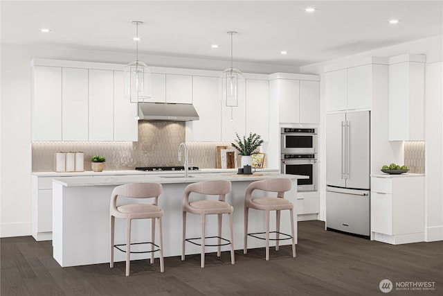 kitchen featuring stainless steel double oven, high end white fridge, light countertops, under cabinet range hood, and a kitchen breakfast bar