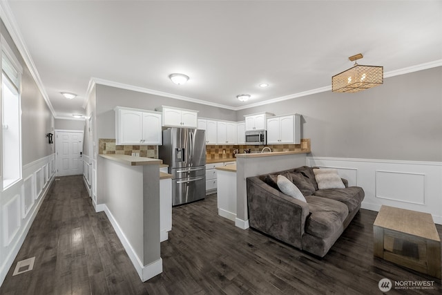 kitchen with appliances with stainless steel finishes, a peninsula, dark wood-style flooring, and white cabinetry