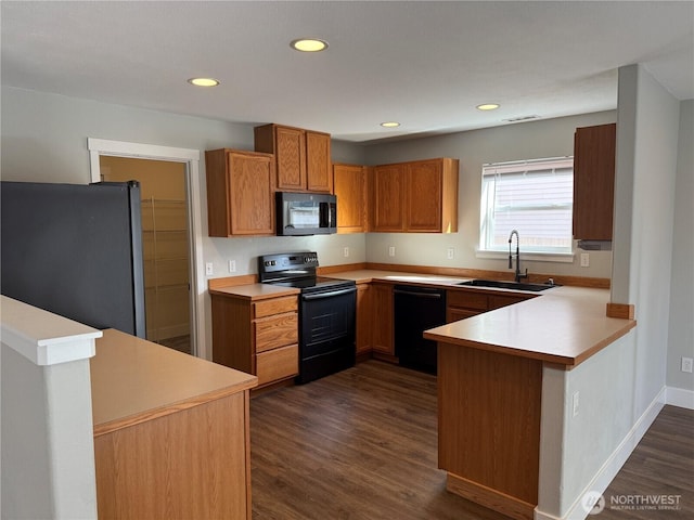 kitchen featuring dark wood finished floors, light countertops, a peninsula, black appliances, and a sink