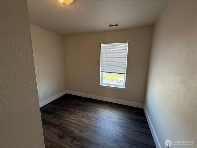 spare room featuring dark wood-style floors, visible vents, and baseboards