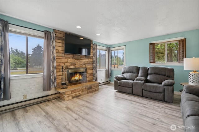 living area featuring a baseboard heating unit, wood finished floors, baseboards, and a fireplace