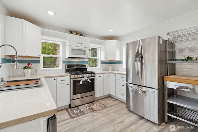 kitchen featuring light wood-type flooring, a sink, white cabinetry, stainless steel appliances, and decorative backsplash