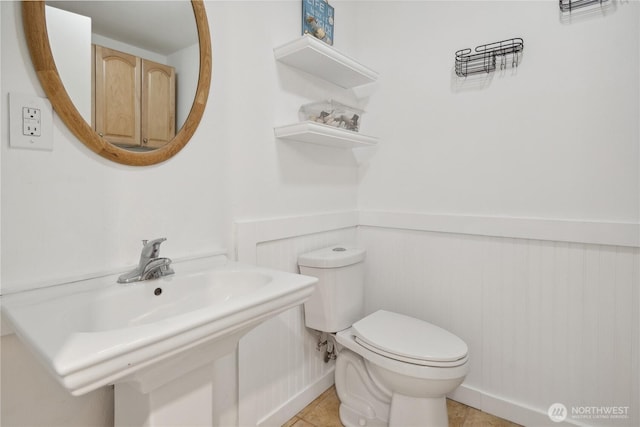 half bathroom with toilet, wainscoting, and tile patterned flooring