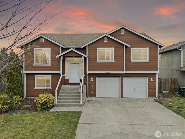 bi-level home with a garage, concrete driveway, and fence