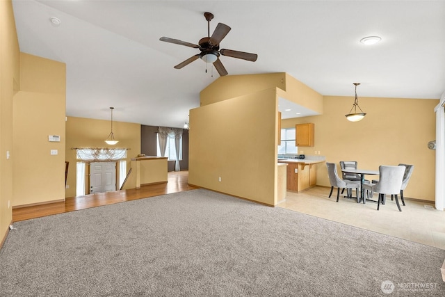 living area featuring a ceiling fan, vaulted ceiling, plenty of natural light, and light colored carpet