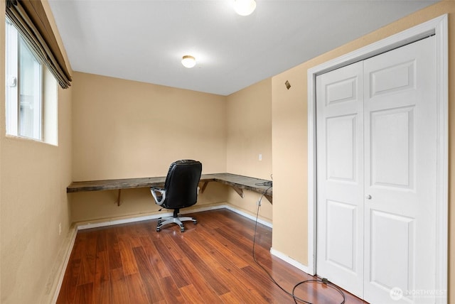 unfurnished office featuring built in study area, dark wood-type flooring, and baseboards