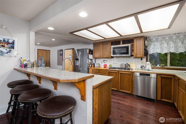 kitchen featuring a kitchen breakfast bar, dark wood-style floors, stainless steel appliances, brown cabinetry, and light countertops