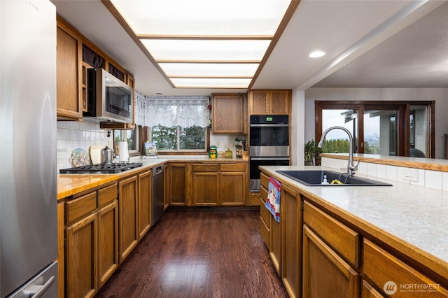 kitchen featuring dark wood finished floors, light countertops, brown cabinets, appliances with stainless steel finishes, and a sink