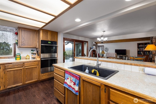 kitchen with light countertops, brown cabinets, stainless steel double oven, and a sink