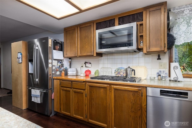 kitchen with backsplash, appliances with stainless steel finishes, brown cabinetry, and light countertops