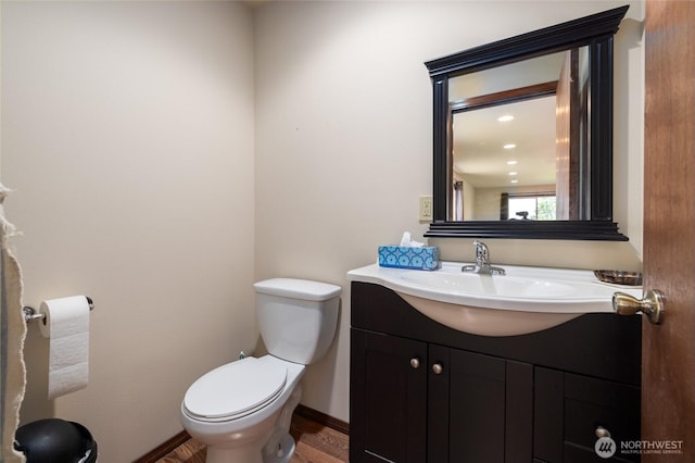 half bathroom with baseboards, toilet, and vanity