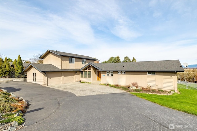 view of front facade with a front lawn, an attached garage, fence, and aphalt driveway