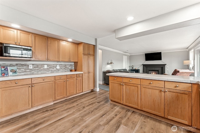 kitchen featuring stainless steel microwave, light wood-style floors, open floor plan, and ornamental molding