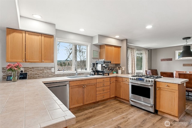 kitchen featuring tile countertops, a peninsula, light wood-style floors, stainless steel appliances, and a sink