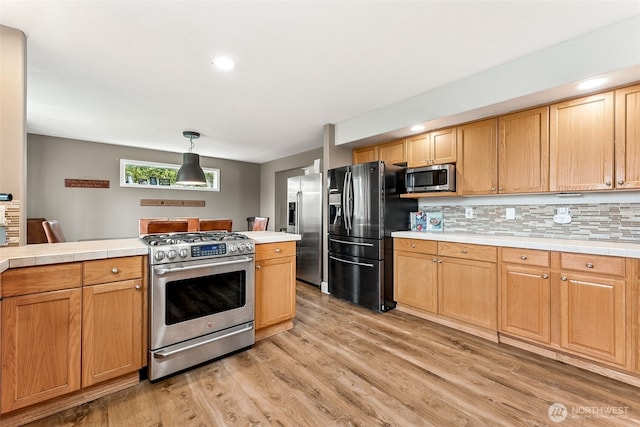 kitchen with backsplash, tile countertops, pendant lighting, light wood-style flooring, and stainless steel appliances